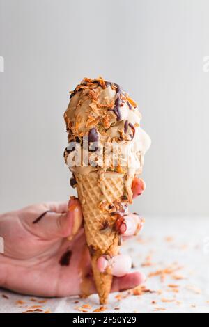 Hand hält eine Waffel Eis Kegel mit schmelzendem Eis gekrönt. Stockfoto