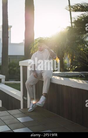 Vertikale Aufnahme des europäischen Mannes in einem weißen Hemd mit Tätowierte Arme sitzen im Freien Stockfoto