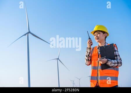 Junge Ingenieurin mit Walkie Talkie, um das System gegen zu überprüfen Windturbinenpark Stockfoto