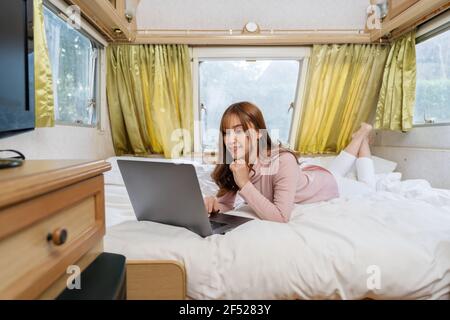 Junge Frau mit Laptop-Computer auf dem Bett eines Wohnmobils Wohnmobil Stockfoto