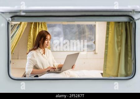 Junge Frau mit Laptop-Computer auf dem Bett eines Wohnmobils Wohnmobil Stockfoto