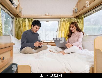 Junges Paar mit Smartphone und Laptop-Computer auf dem Bett Ein Wohnmobil Wohnmobil Wohnmobil Stockfoto