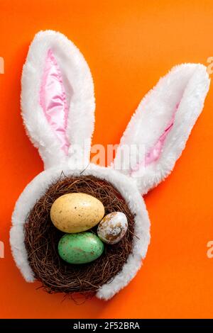 Frohe ostern und Frühling Meme Konzept mit entzückenden Hasen Ohren Auf einem Vogelnest mit bunten Eiern gegen eine Orange Hintergrund Stockfoto