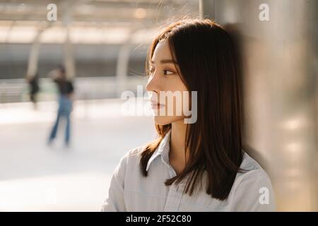 Porträt einer nachdenklichen jungen asiatischen Geschäftsfrau, die sich gegen das Gebäude lehnt Säule schaut weg beim Tagträumen und Nachdenken über neue Ideen Stockfoto
