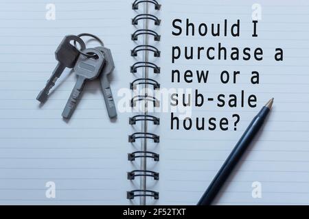 Text auf Notizbuch mit Hausschlüssel und Stift geschrieben - Sollte ich ein neues oder Unterhaus kaufen Stockfoto