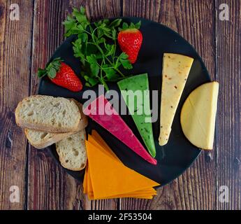 Draufsicht auf verschiedene holländische und niederländische Käsesorten auf dem Teller und Brot und Obst auf Holzkulisse. Stockfoto