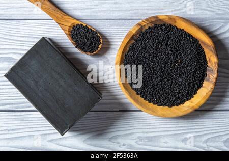 Nigella sativa Samen Draufsicht Fotografie, in einem Holzteller und Holzlöffel. Auf einem hölzernen grauen Tisch. Stockfoto