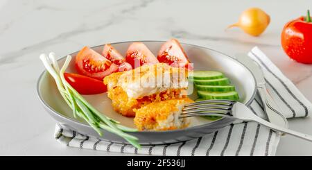 Gebratene panierte Fischfilets mit Gurkenamanttomaten, die aus nächster Nähe auf einem Teller serviert werden. Stockfoto