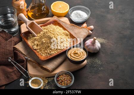 Ein kulinarisches Stillleben mit Senfpulver und Zutaten mit Platz zum Kopieren auf braunem Hintergrund. Seitenansicht, horizontal. Stockfoto