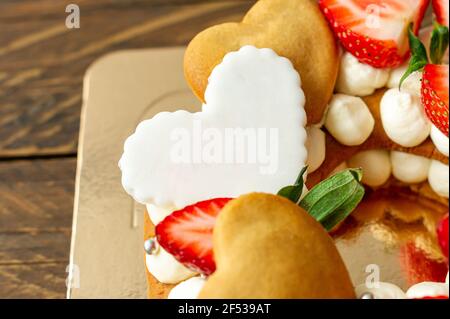 Biskuitkuchen mit Erdbeeren, rosa Milchschokolade, Silberstreuseln, Vanillecreme und herzkranken Keksen aus nächster Nähe. Sommer süßes Dessert für bi Stockfoto
