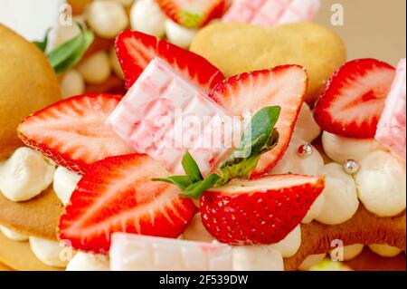 Biskuitkuchen mit Erdbeeren, rosa Milchschokolade, Silberstreuseln, Vanillecreme und herzkranken Keksen aus nächster Nähe. Sommer süßes Dessert für bi Stockfoto
