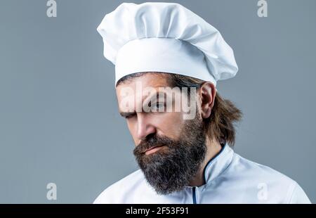 Kochmütze. Selbstbewusster bärtiger Chefkoch in weißer Uniform. Porträt eines ernsthaften Koch Koch. Bärtiger Koch, Köche oder Bäcker. Bärtige männliche Köche isoliert Stockfoto