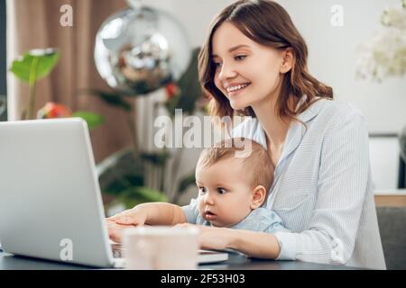 Mama mit kleinem Kind sitzt am Laptop Stockfoto