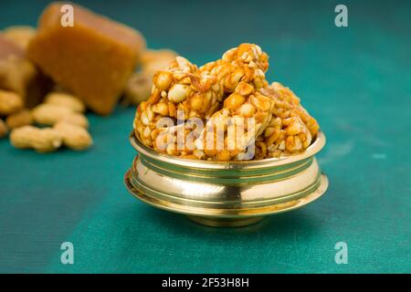 Peanut Bar, knusprig süß Peanut Bar, die sehr gesund ist und Leckerer Snack, in einem Messinggefäß mit Erdnuss und Jaggery arrangiert Auf der dunkelgrünen Farbe Stockfoto