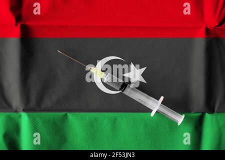 Konzept der laufenden Bemühungen Libyens, COVID-19-Impfstoff mit einer gebrauchsfertigen Spritze auf libyscher Flagge zu liefern und zu verteilen. Stockfoto