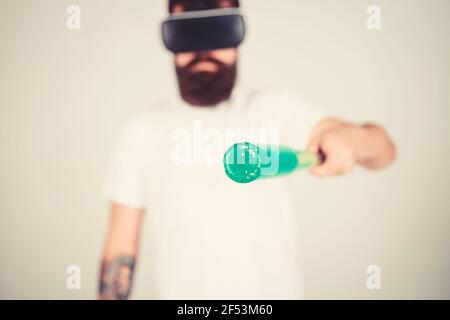 Mann mit Bart in VR-Brille hält Baseballschläger, grauer Hintergrund. VR Sportsman Konzept. Kerl mit VR-Brille spielen Baseball. Hipster auf konzentriert Stockfoto