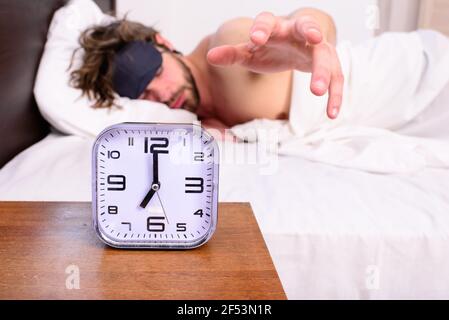Wecker am Nachttisch Mann schläfrig unrasiert bärtigen Gesicht Schlaf Augenmaske Hintergrund. Mann in Augenmaske besser schlafen. Tipps für gesunden Schlaf. Typ versuchen Stockfoto