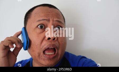Ein asiatischer Mann mit kahlem Haar telefoniert mit einem alten Telefon mit seltsamem Ausdruck Stockfoto