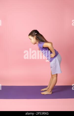 Ganzkörperportrait eines Mädchens, das Yoga in der Ardha Uttanasana macht oder halb nach vorne stehend, isoliert auf einem rosa Hintergrund Stockfoto