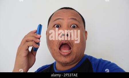 Ein asiatischer Mann mit kahlem Haar telefoniert mit einem alten Telefon mit seltsamem Ausdruck Stockfoto