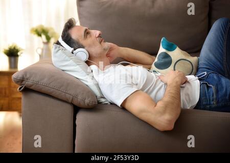 Entspannter Mann, der auf einem Sofa mit Kopfhörern liegt Zur Musik, die krachend starrt Stockfoto