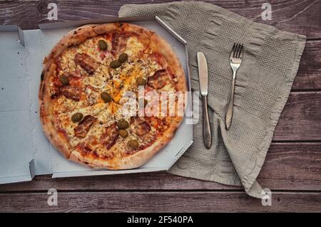 Leckere Pizza zum Mitnehmen auf einem Holztisch. Zugeschnittenes Foto von Händen, die ein Stück Pizza nehmen Stockfoto