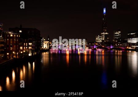 Der Blick entlang der Themse bis zur London Bridge erhellt Nacht mit orangefarbenen und violetten Lichtern Stockfoto