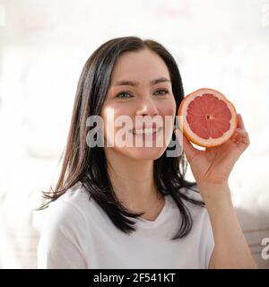 Lächelnde Frau in blauem Hemd, die Grapefruit in einer Küche hält Stockfoto