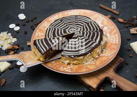 Schokolade in Scheiben geschnitten esterhazy Kuchen mit Sahne, Zuckerguss, Nüsse, Zimt und Mandeln Nahaufnahme von oben auf einem orange-braunen Teller, auf einem hölzernen Wildschwein Stockfoto