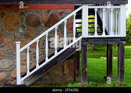 Holztreppe mit weißem Geländer, die zum zweiten Stock eines Steinhauses im Park des Landgutes Petrowskoje in Puschkin Gory führt. Stockfoto