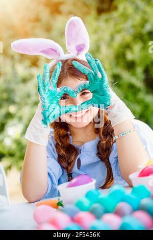 Portrait eines niedlichen kleinen Mädchens gekleidet als Osterhase Farben Eier für Christian Holiday. Zeigt Liebe mit Gesten. Frohe Ostern. Stockfoto