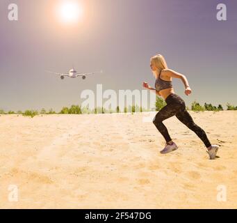 Das Flugzeug fliegt im Himmel unter der Sonne und ein Sportmädchen läuft auf dem Sand in der Wüste. Bewegung in der Natur Stockfoto