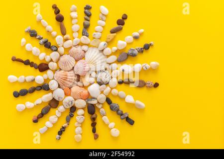Abstrakte Sonne aus Meereskieseln und Muscheln auf gelbem Hintergrund, Kopierraum, Urlaub am Meer oder Meer Stockfoto