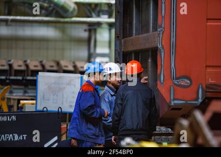 Ekibastuz, Region Pavlodar, Kasachstan - 28. Mai 2012: Eisenbahnwagenkollenwerk. Qualitätskontrolle der Montage. Zwei Arbeiter und ein Ingenieur sprechen. Stockfoto