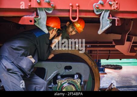 Ekibastuz, Region Pavlodar, Kasachstan Mai 28 2012: Eisenbahnwagentauschwerk. Zwei Arbeiter unter dem Auto. Stockfoto