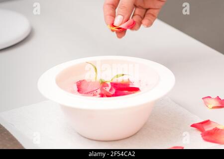 Die weiblichen Hände der Kosmetikerin bereiten das Maniküre-Bad mit Rot und Rosa vor rosenblüten auf dem Tisch im Spa Stockfoto