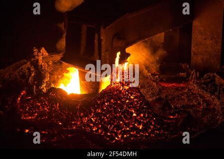 Metallurgische Anlage. Eimer mit flüssigem geschmolzenem Metall. Funken aus heissem Metall und oranger Flamme. Metalllegierungsanlage. Stockfoto