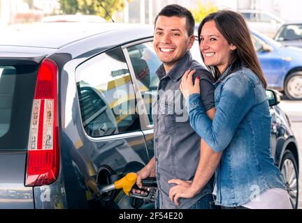 Glückliches Paar an der Tankstelle, das Benzin an der Gaspumpe pumpt. Porträt des jungen Mannes und der Frau des Mannes, der modernes Auto am Benzintank füllt Stockfoto