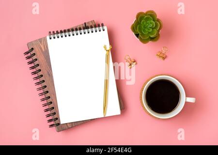 Notizblock öffnen, Tasse Kaffee, goldener Stift auf rosa Hintergrund, Spiralnotizbuch auf Tisch Business, Planung, Bildungskonzept Draufsicht Flat Lay. Stockfoto