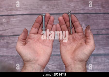 Zwei Schrauben und Muttern in den Händen der arbeitenden Männer. Stockfoto