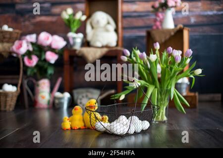 Korb mit weißen ostereiern auf dem Vordergrund und eine Vase mit Blumen, Enten und osterdekoration auf dem Hintergrund Stockfoto