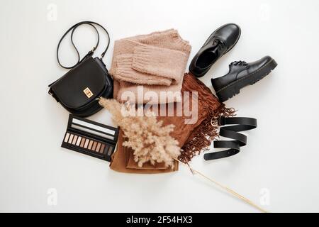 Mode Basis weibliche gefaltete Kleidung in beige braune Farbe Outfit gesetzt. Stoffschuhe im lässigen Stil, Strickpullover. Flat Lay Kleidung Kosmetik auf weiß Stockfoto