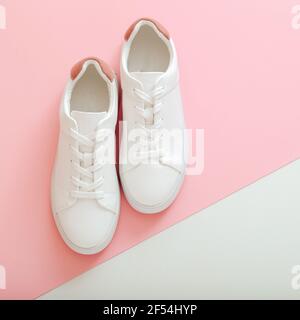 Weiße Sneakers, weibliche weiße Lederschuhe mit Schnürsenkeln auf rosa Hintergrund. Paar stilvolle Sneaker bequeme Sportswear Hipster Damenschuhe. Oben Stockfoto