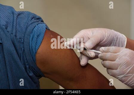 Eine Krankenschwester, die Einweghandschuhe trägt, die einen covid-19-Impfstoff injiziert Mann Arm Stockfoto