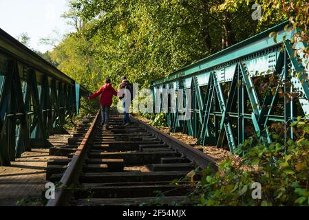 Vater und Sohn gehen auf verlassenen Eisenbahn im Herbstwald in Französisch Landschaft. Rückansicht. Natürliches Lifestyle-Konzept. Familienurlaub Hintergrund. Stockfoto