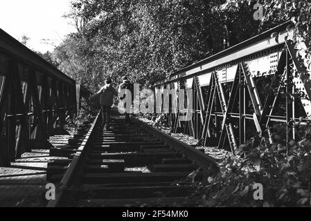 Vater und Sohn gehen auf verlassenen Eisenbahn im Herbstwald in Französisch Landschaft. Rückansicht. Schwarz weiß retro Foto. Selektiver Fokus. Stockfoto