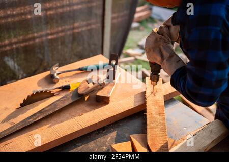 Zimmermann bohrt Holz ein Loch mit einem elektrischen Bohrer. Stockfoto