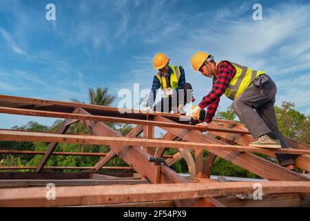 Asiatische Bauarbeiter installieren neues Dach, Dachbedachung Werkzeuge, elektrische Bohrmaschine auf neuen Dächern von Holzdachkonstruktion verwendet, Teamwork Konstruktionskonzept. Stockfoto