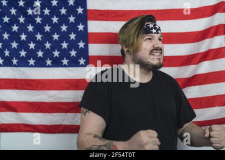 Bärtiger kaukasischer Mann mit einem Bandana, der lächelt, während er sich darin posiert Vorderseite der US-Flagge Stockfoto