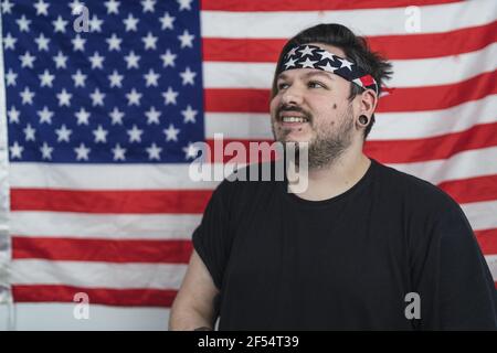 Bärtiger kaukasischer Mann mit einem Bandana, der lächelt, während er sich darin posiert Vorderseite der US-Flagge Stockfoto